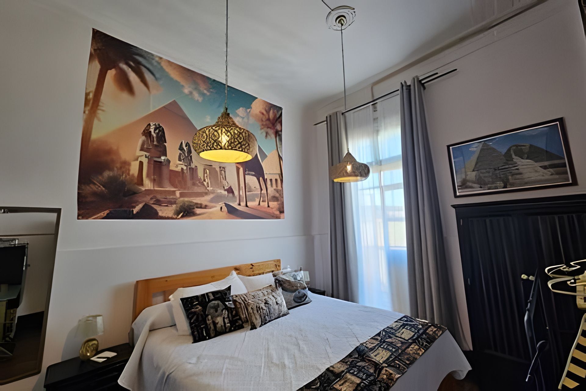 Habitación de hotel con una cama grande, un cuadro colgado en la pared, una lámpara de techo y una ventana con cortinas.