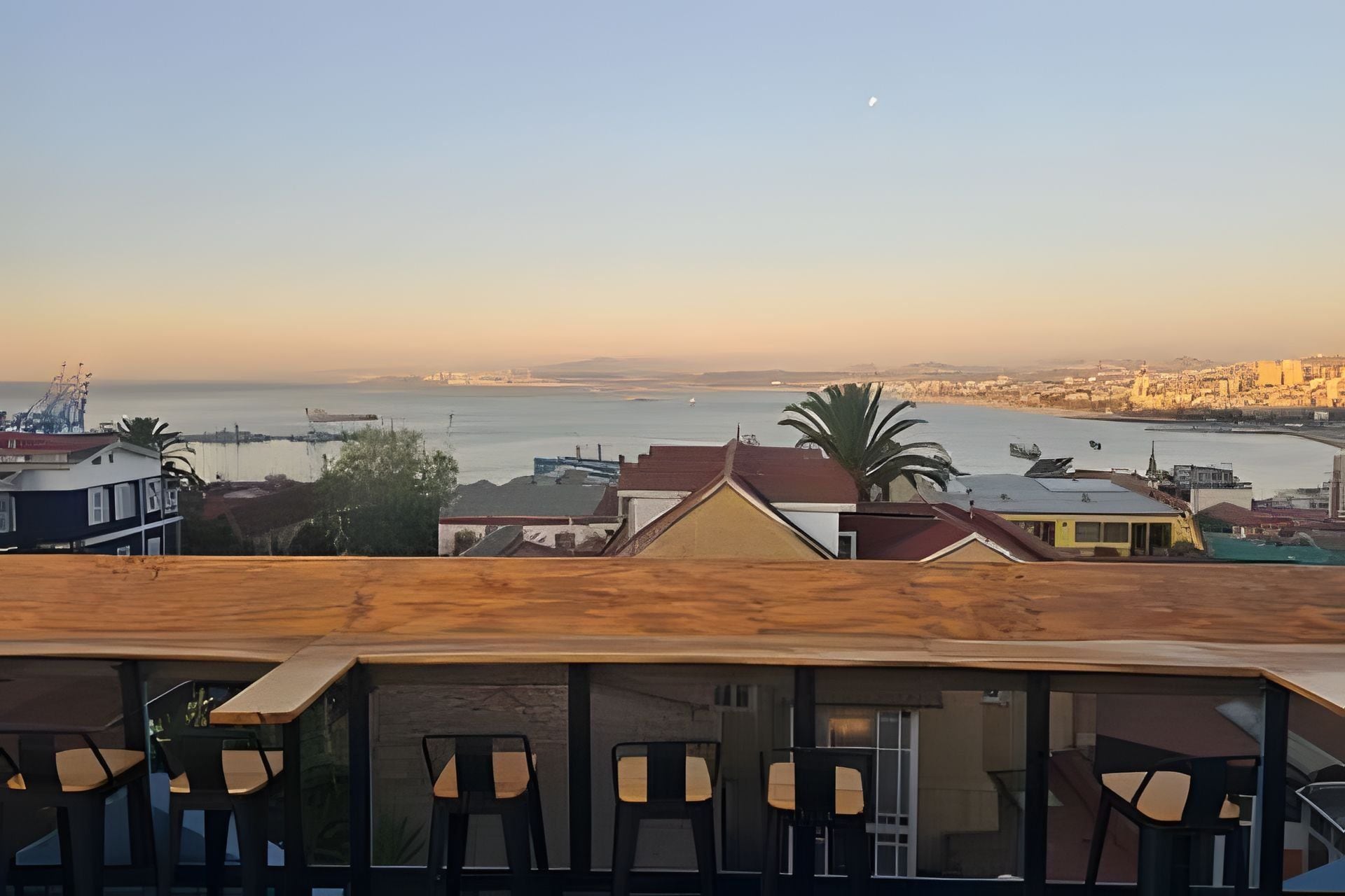 Una terraza con sillas, vista al mar y edificios al fondo.
