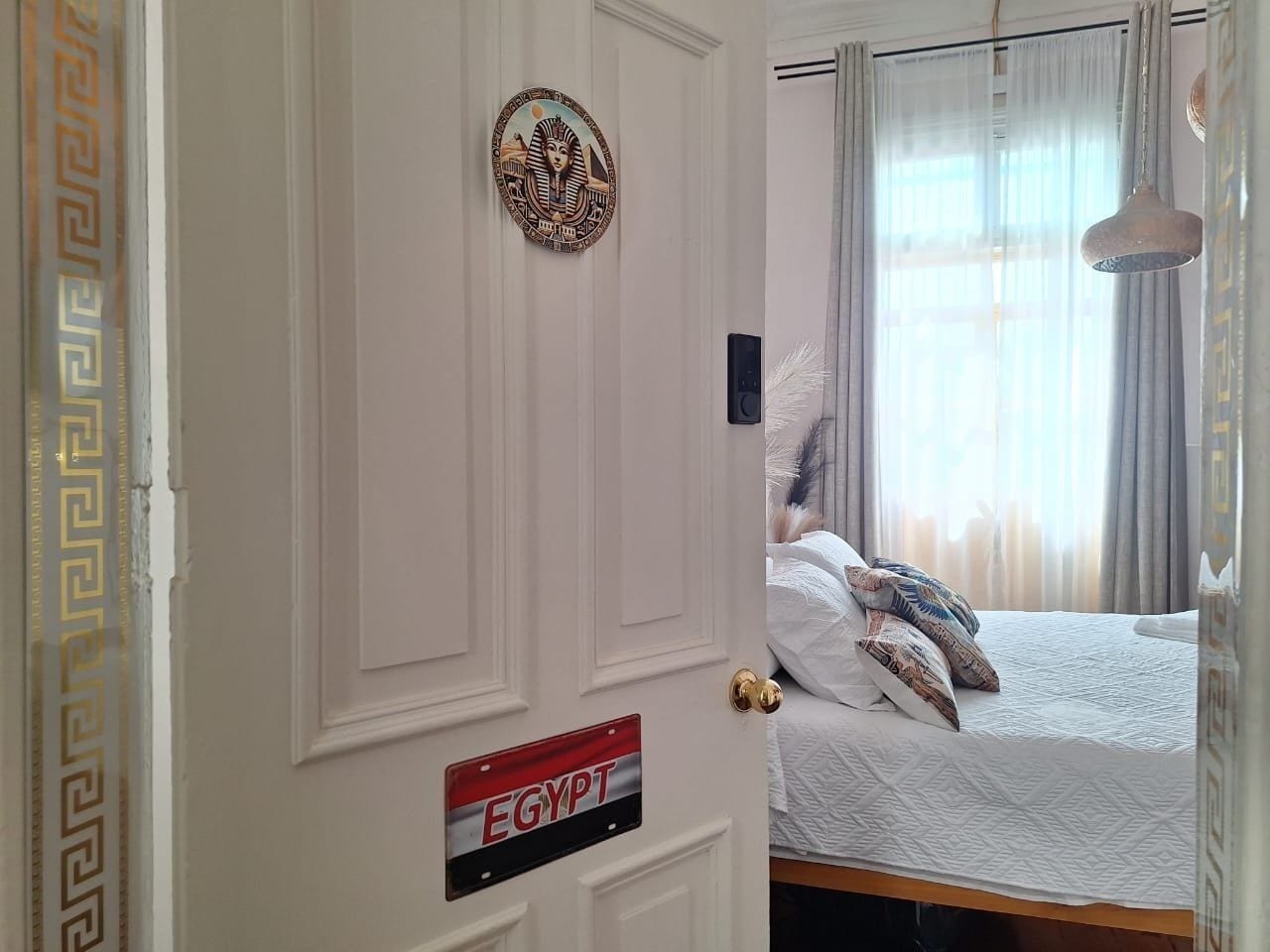 A room with a bed, a door with a sign reading 'EGYPT,' and a decorative wall piece.