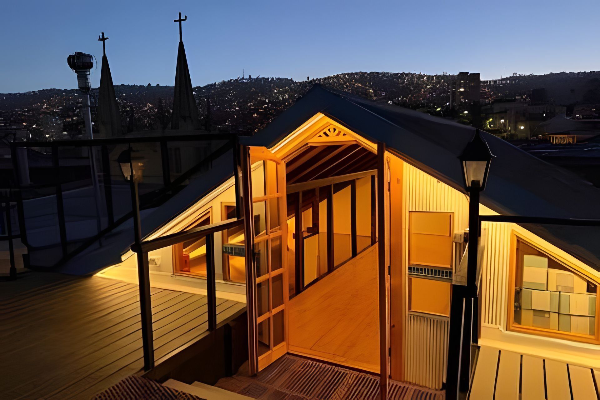 Una pequeña construcción de techo triangular con una terraza de madera y una escalera que lleva a una puerta.
