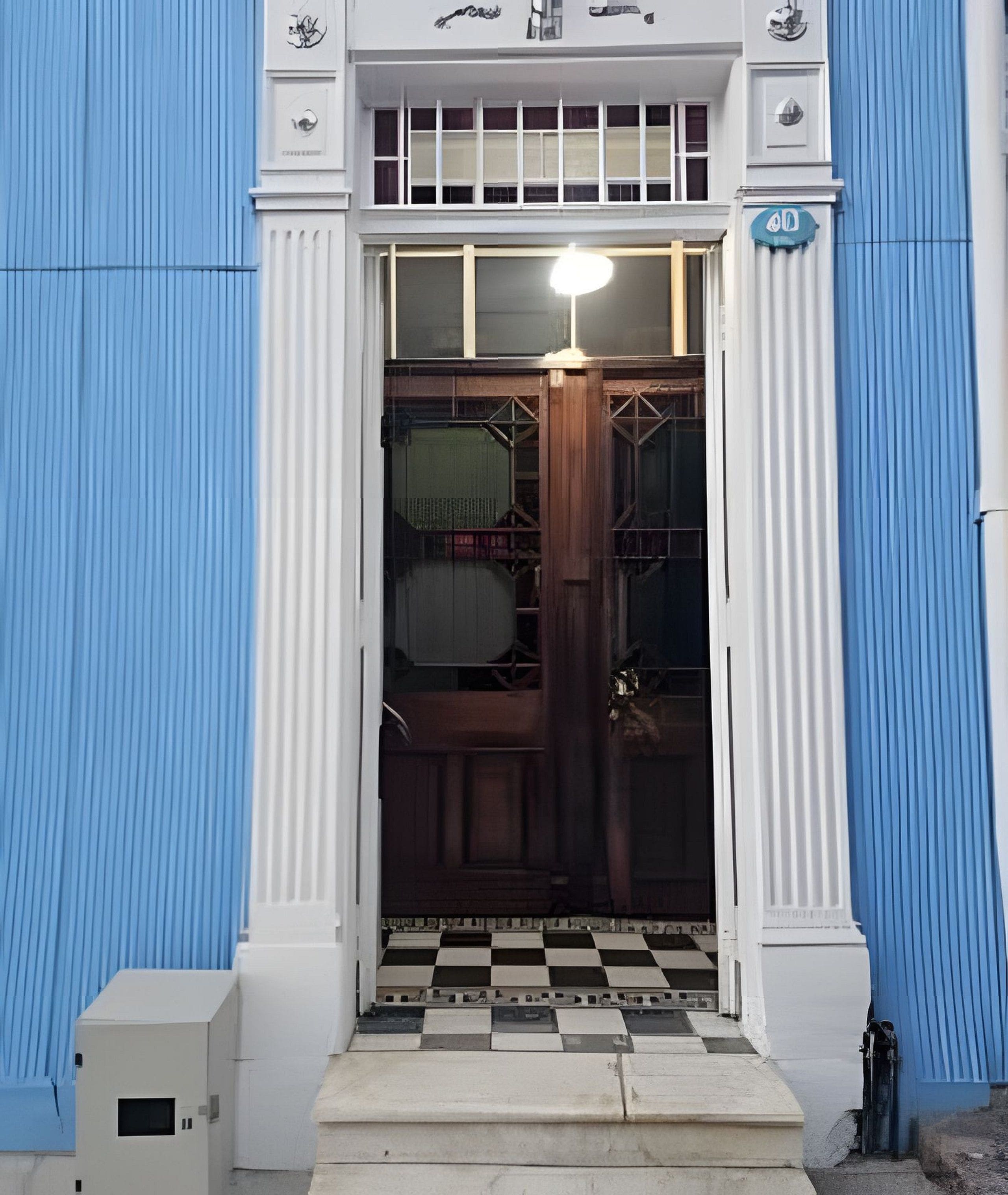 Entrada de un edificio con suelo a cuadros, una puerta con apliques de luz y una decoración azul y blanca.