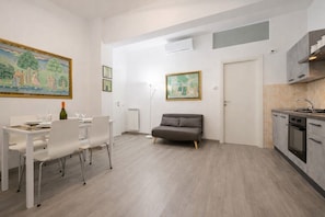 Um apartamento moderno com área de jantar, sofá, cozinha e duas pinturas nas paredes.