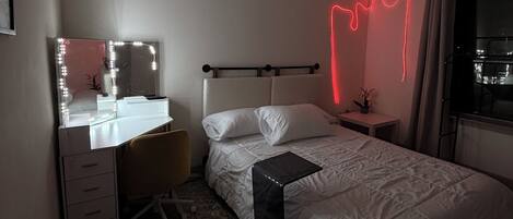 A bedroom with a bed, a desk with a mirror, a ceiling fan, and a nightstand.