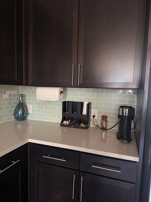 A kitchen with dark wooden cabinets, a countertop, a paper towel holder, a spice jar, and a coffee maker. - Luxury Skyline Condo. Walk to Deep Ellum, Downtown or Farmers Market (Dallas)
