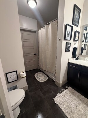 Een badkamer met toilet, douchegordijn, vloerkleed en ingelijste foto’s aan de muur.