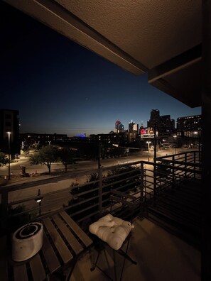 Ein Balkon mit Blick auf eine Stadtlandschaft im Abendlicht, mit Gebäuden und einem entfernten Riesenrad.