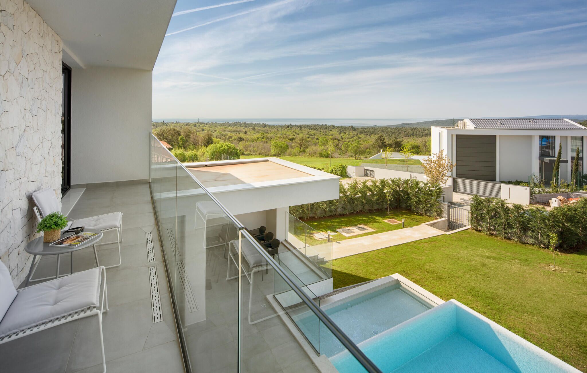 Un balcon moderne avec une balustrade en verre, une piscine et une vue sur un paysage verdoyant.