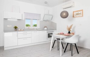 Eine moderne Küche mit weißen Schränken, ein Essbereich mit weißem Tisch und Stühlen sowie ein Blick auf Grünflächen außerhalb.
