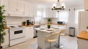 A modern kitchen with white cabinetry, a central island with bar stools, a stainless steel refrigerator, and a microwave. - Modern 3BR Home Near Montreal | Free Parking (Longueuil)