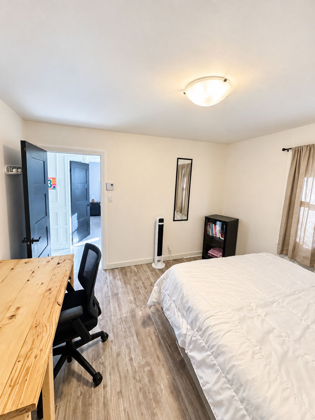 A room with a bed, a desk, a chair, a bookshelf, and a door leading to another room.