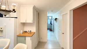 A narrow hallway with a kitchen area on the left, featuring cabinets, a countertop, and a chandelier. - Modern 3BR Home Near Montreal | Free Parking (Longueuil)