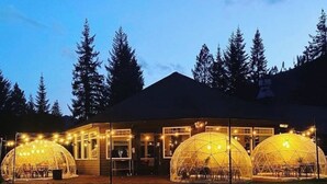 Un edificio con due grandi strutture a cupola trasparente, presumibilmente per eventi, con luci a tendina e tavoli all'esterno.