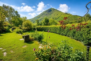 Ein üppiger Garten mit einem Kiesweg, einem Berg im Hintergrund und einem klaren Himmel.
