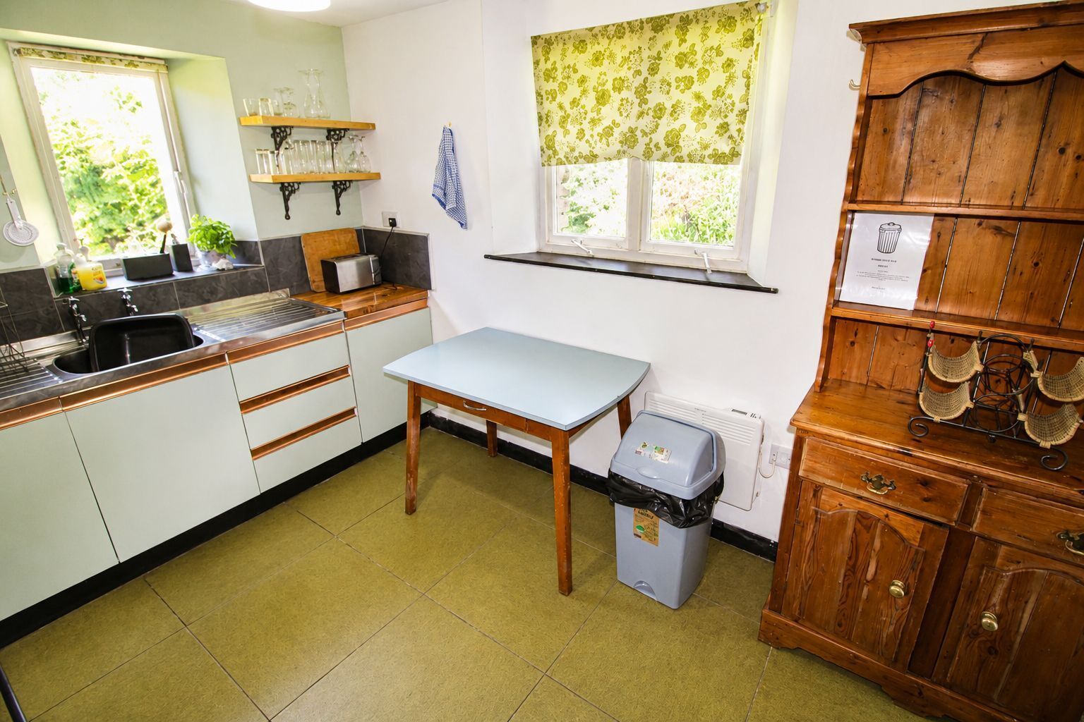 A kitchen with a sink, countertop, table, and a trash bin.