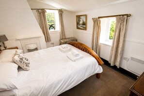 Ein Schlafzimmer mit einem Bett, einem Sessel, einem Kamin und zwei mit Vorhängen versehenen Fenstern.