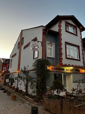 A building with a sign indicating it is a hotel and an apartment. There are potted plants and a wooden bench outside. - Karaçam Apart Otel (Kastamonu)