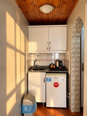 Una cuineta compacta amb armaris blancs, un rentamiques integrat, un refrigerador petit i un gresol.