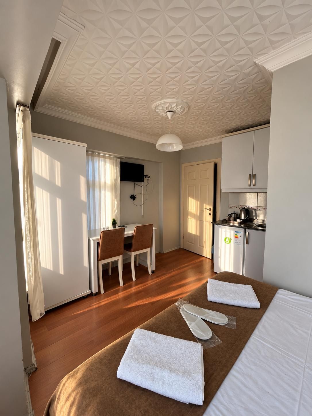 A hotel room with a bed, a desk, a chair, a kitchenette, and a bathroom.