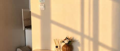 Un comedor con una mesa blanca y dos sillas marrones, un florero con flores, y una mesita con un recipiente de vidrio.