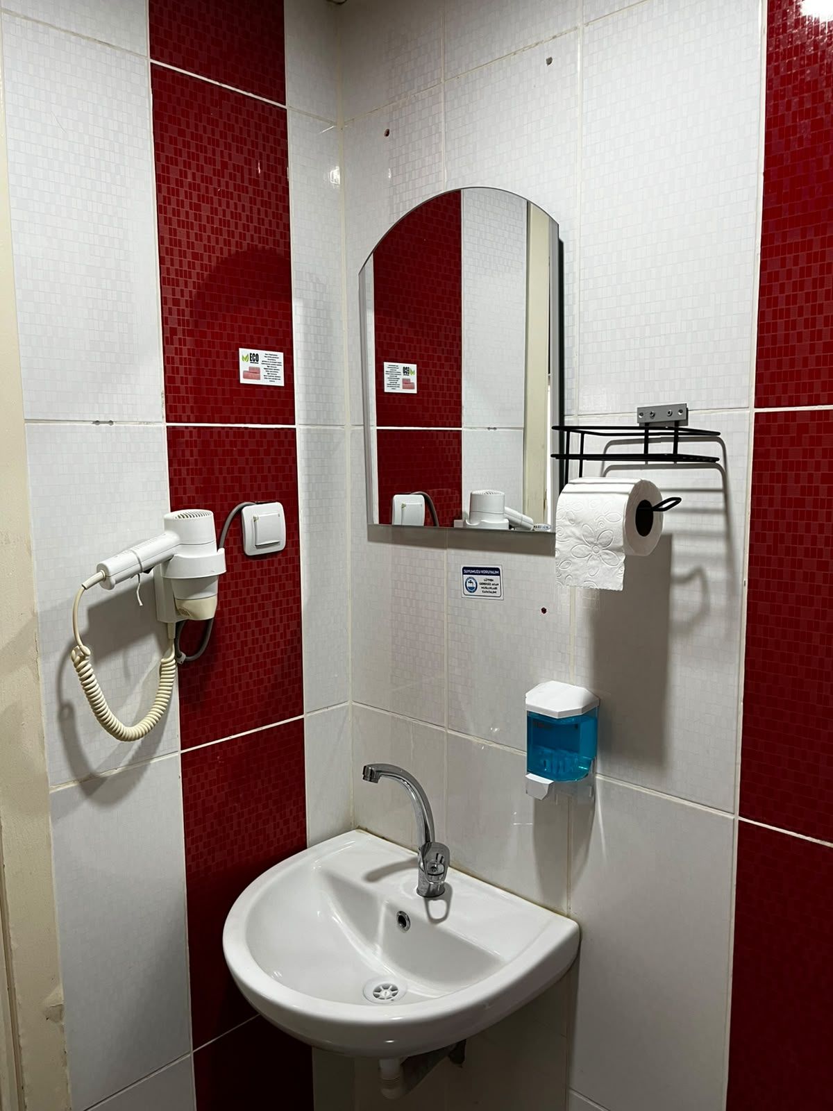 Een badkamer met een wit wastafelmeubel, rode betegelde muren, een spiegel, een handdoekhouder en een handdroger.