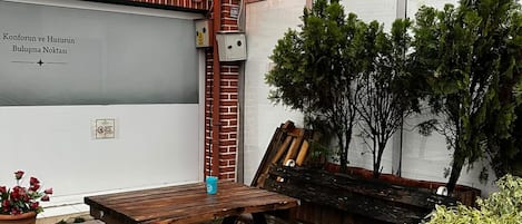 Un espacio al aire libre con mesas y bancos de madera, una planta en maceta y un letrero de hotel.