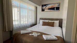A hotel room with a large bed, a painting on the wall, and a window with curtains.