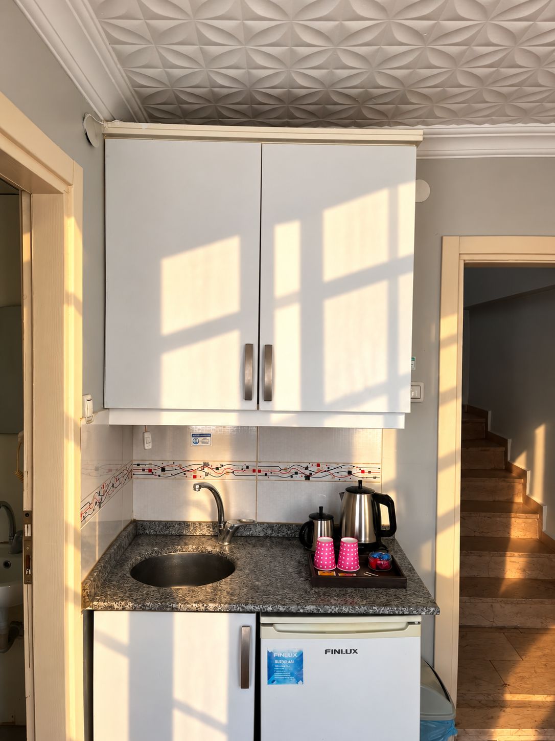 A compact kitchen with white cabinets, a granite countertop, a sink, and a built-in refrigerator.