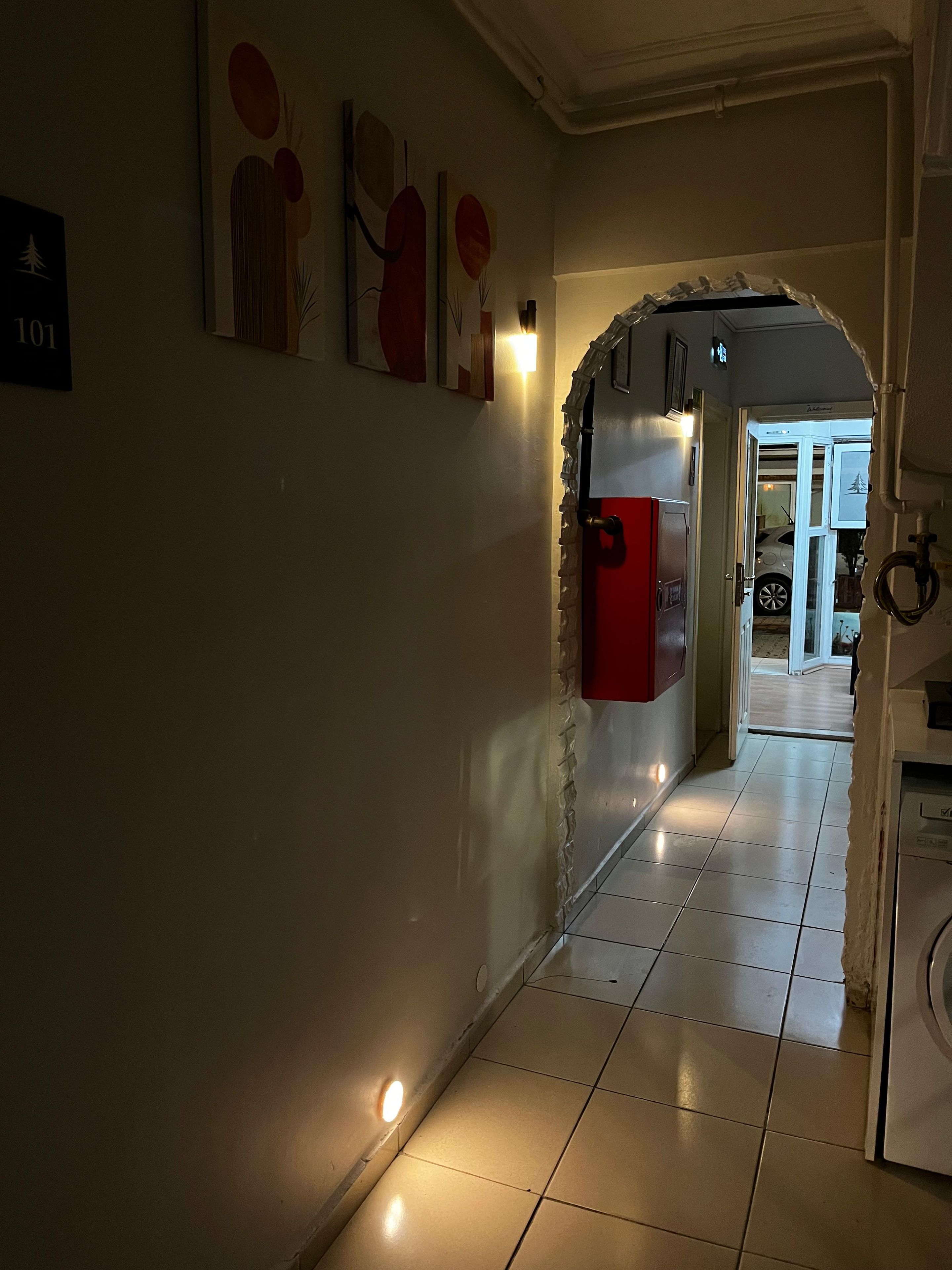 A hallway with a tiled floor, a red door, and a wall-mounted light fixture.