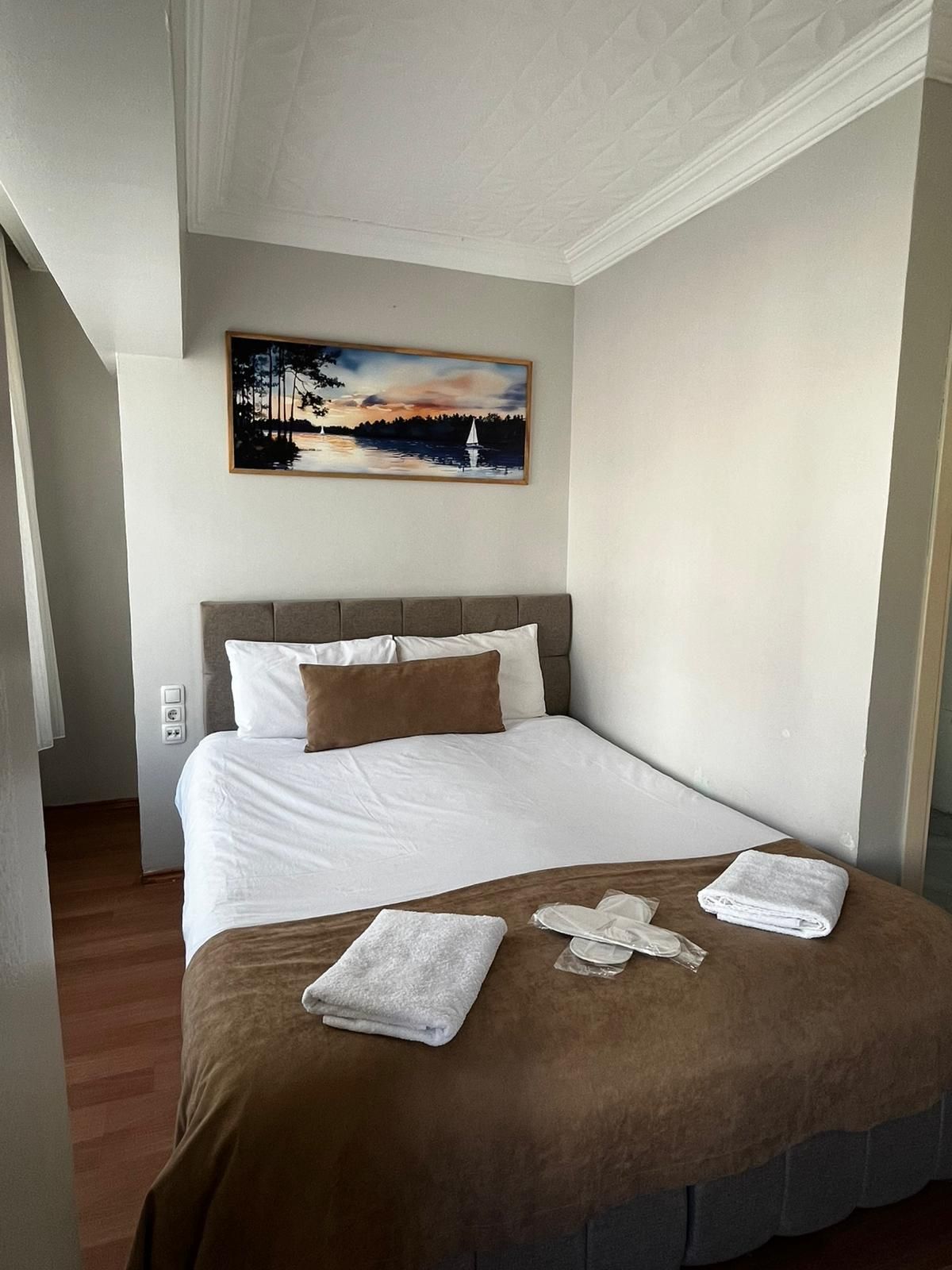 A hotel room with a bed, a painting above it, and a wooden floor.