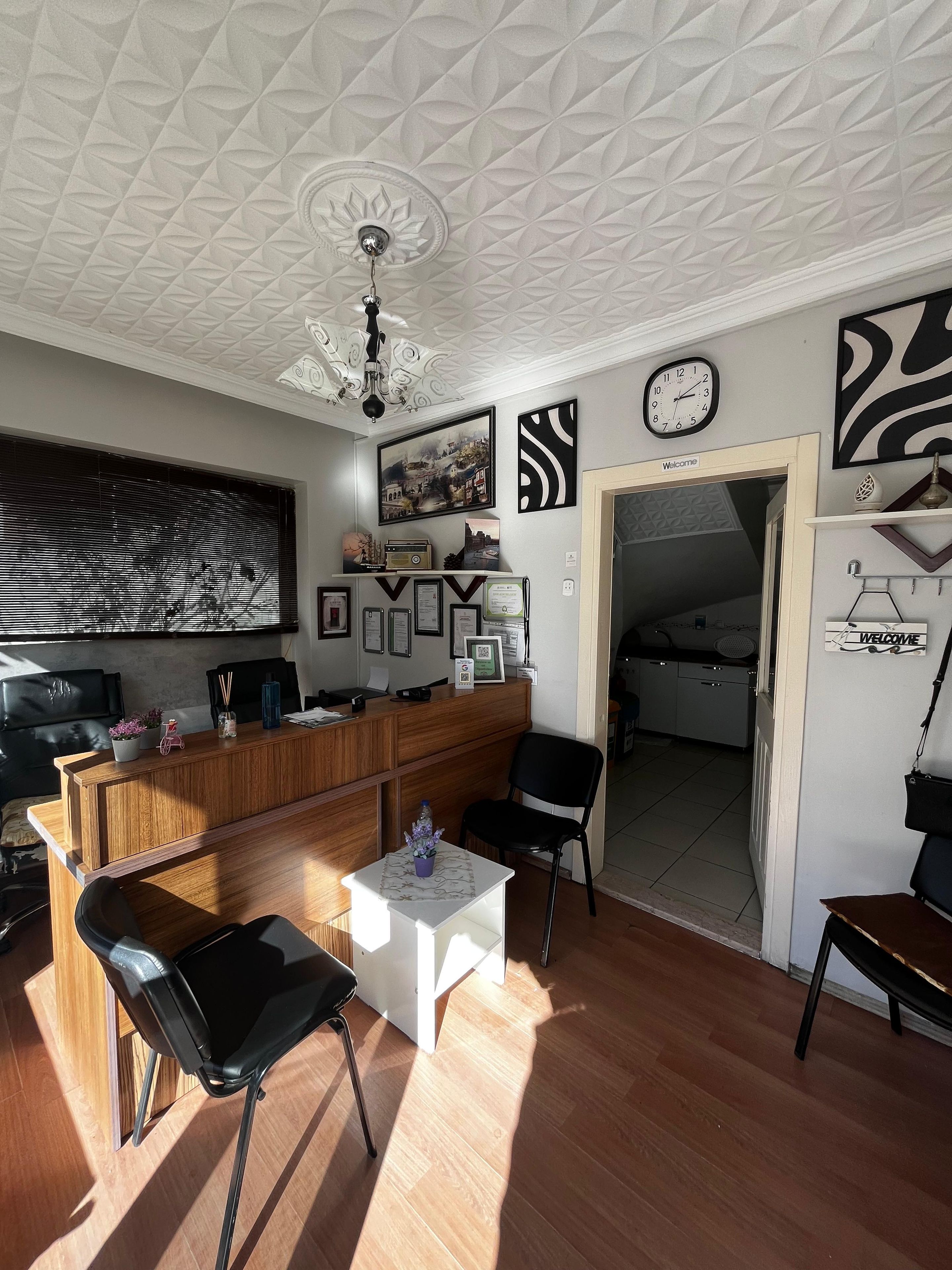 Una sala de estar moderna con un mostrador de recepción de madera, sillas negras, una mesa de centro blanca y un ventilador de techo.