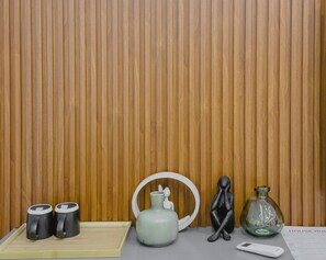 A wooden panel wall, a tray with two black mugs, a white vase, a black sculpture, a glass bottle, and a remote control on a table. - The Regent Spacious Cozy 1 Bedroom (Accra)