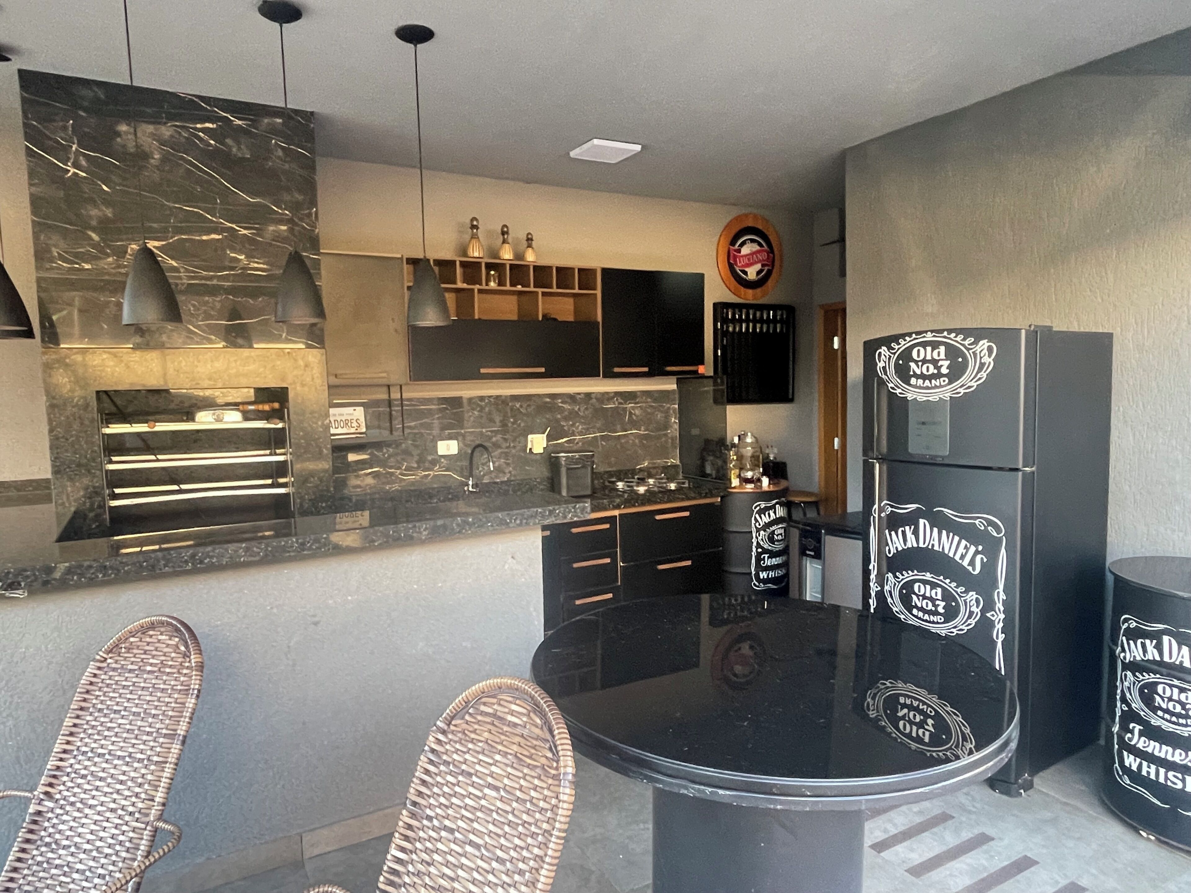 Une cuisine moderne avec un plan de travail noir, des appareils électroménagers intégrés et un coin repas doté de chaises en osier.