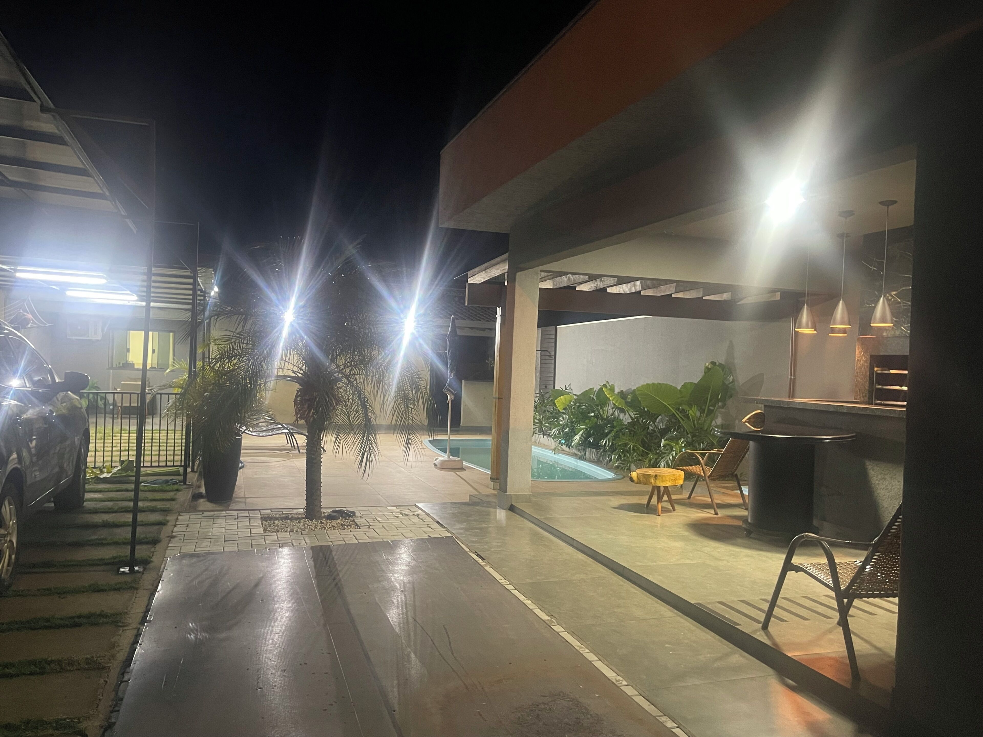 Área de varanda externa com piscina, área de estar e um carro estacionado perto.