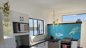 Een moderne keuken met witte kasten, een centraal eiland met krukken, een fornuis en een groot raam.