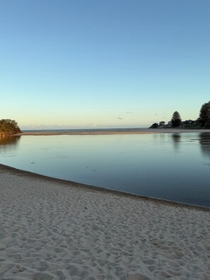 A beach with a calm water body, sandy shore, and some trees in the background.