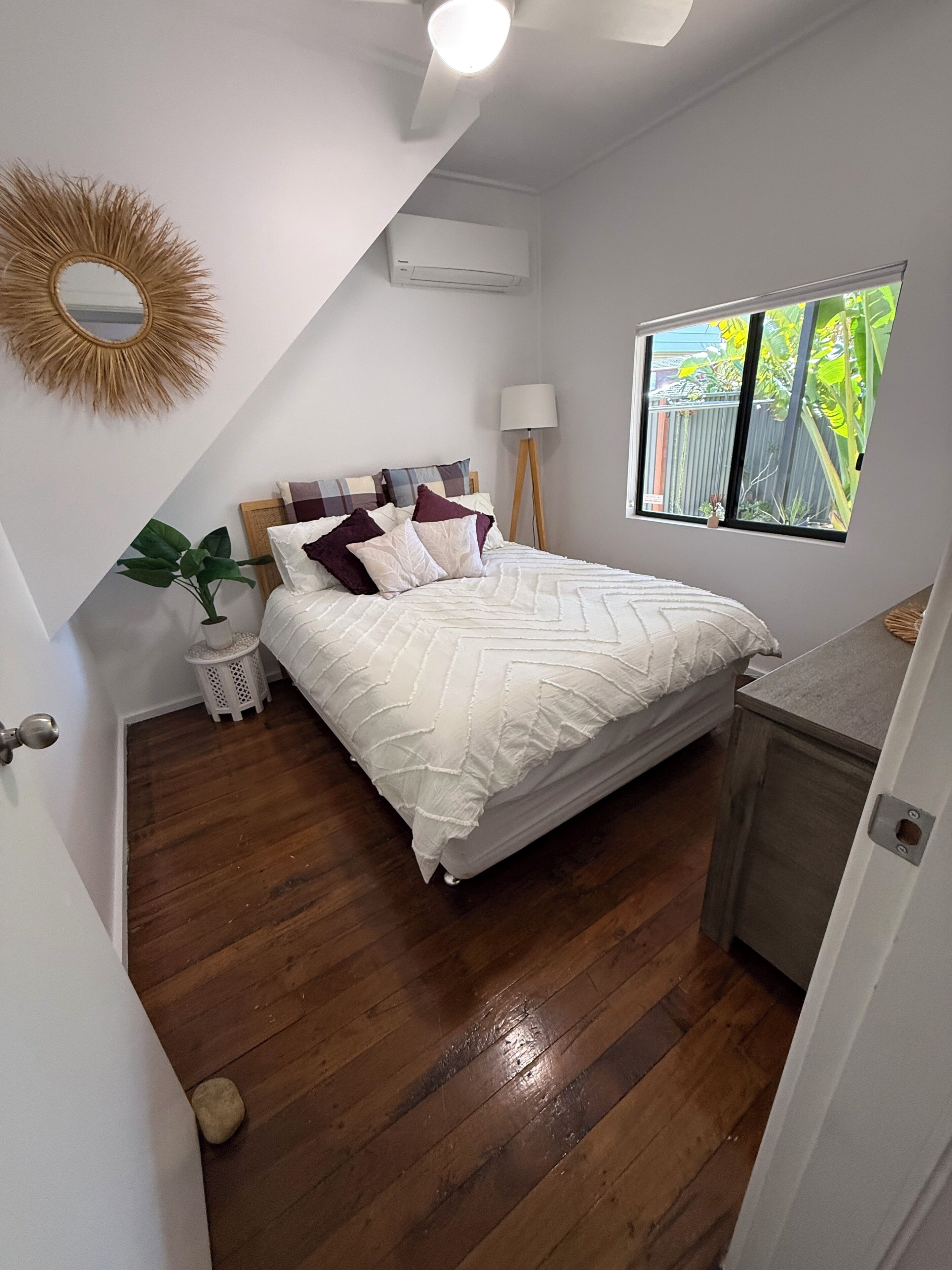 Et soveværelse med seng, senget lampe, et vindue med udsigt, en loftventilator og en aircondition.