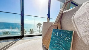 Quarto com uma grande janela com vista para o oceano, uma guitarra e um livro intitulado 'Blue Mini'.