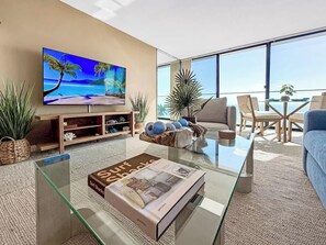 Un saló modern amb un televisor gran, una taula de cafè de vidre i vista a l'oceà.