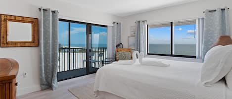 Ein Schlafzimmer mit einem großen Bett, zwei Fenstern mit Meerblick, einem Balkon und einem Nachttisch aus Holz.