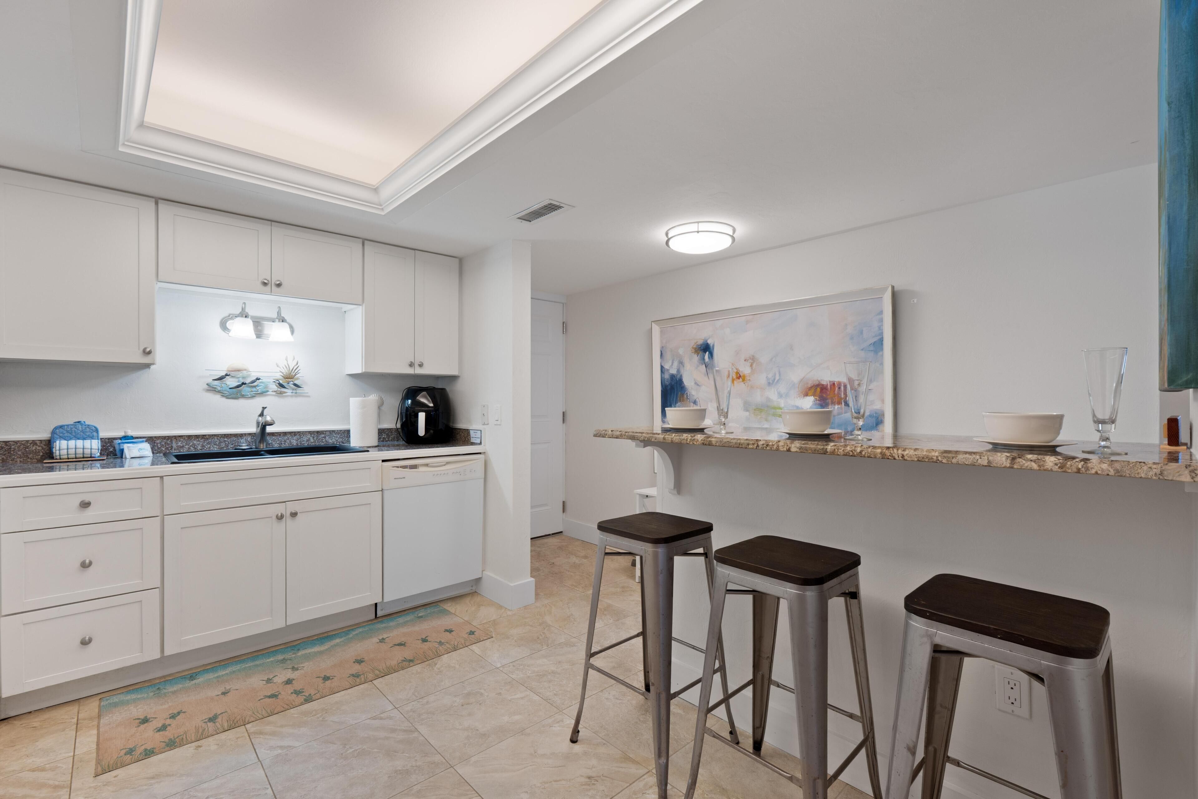Una cocina moderna con muebles blancos, una encimera con una cafetera y un cuadro en la pared.