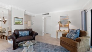 Ein Wohnzimmer mit einem braunen Ledersofa, einem Glastisch und einem blau gemusterten Teppich.