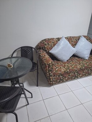 A room with a floral sofa, two white pillows, a glass-top table, and a black chair.
