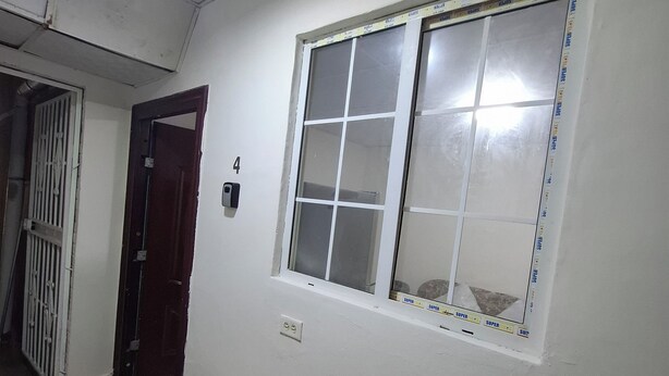 A hallway with a tiled floor, a window with a grid pattern, a door with a number plate, and a wall-mounted light fixture. - Private room in Panama City, near the airport (Panama)