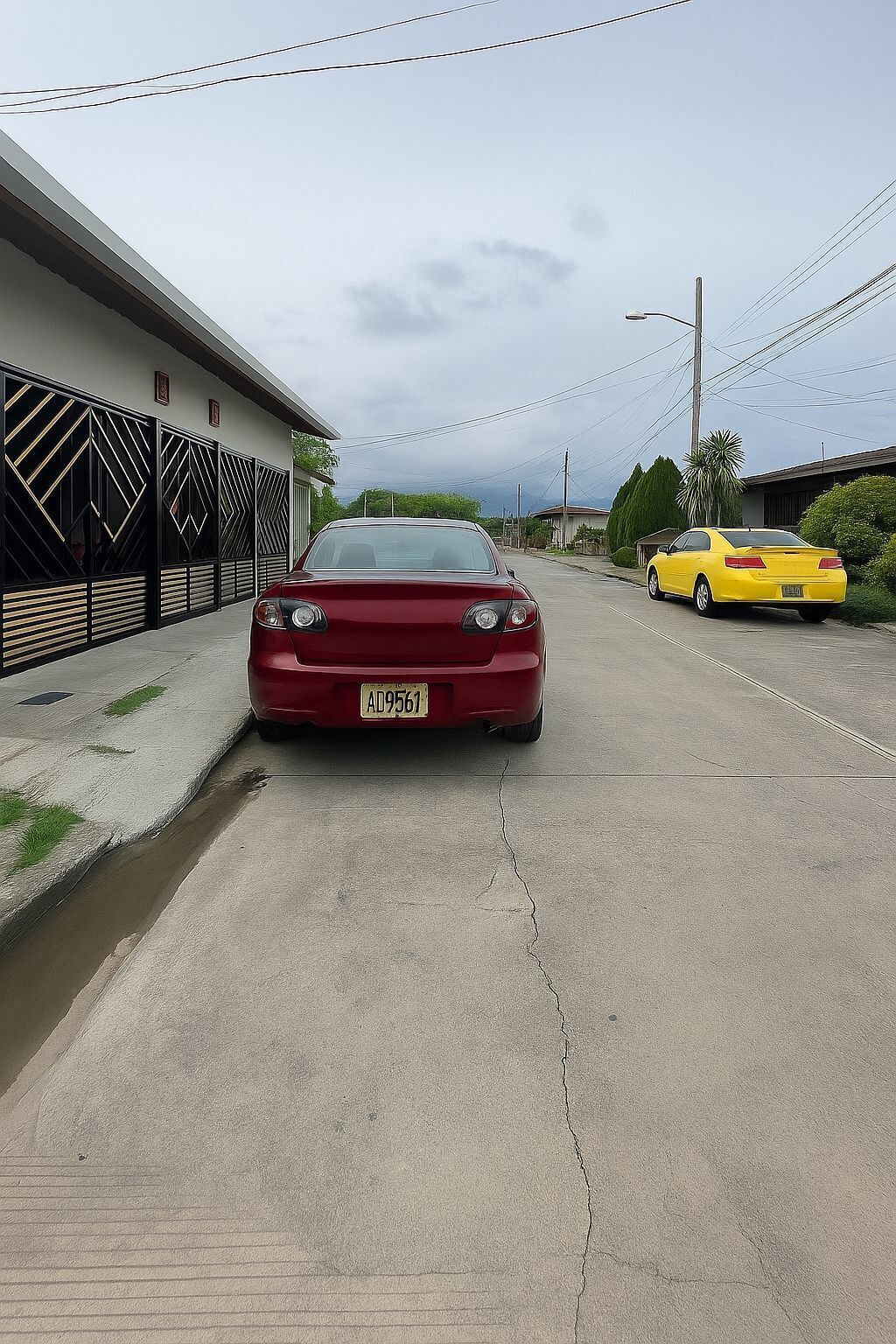 Un coche rojo estacionado en una calle con un edificio a la izquierda y un coche amarillo a la derecha.
