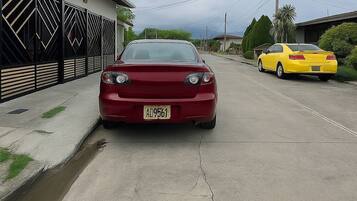 Un coche rojo estacionado en una calle con un edificio a la izquierda y un coche amarillo a la derecha.