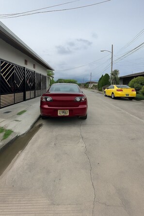 A red car parked on a street with a building on the left and a yellow car on the right.