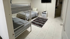 A room with bunk beds, a flat-screen TV, an air conditioning unit, a bedside table with a lamp, and a patterned rug. - Private room in Panama City, near the airport (Panama)