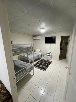 A room with bunk beds, a flat-screen TV, an air conditioning unit, a bedside table with a lamp, and a patterned rug. - Private room in Panama City, near the airport (Panama)