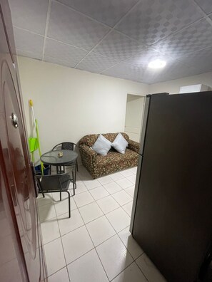 A compact room with a tiled floor, a sofa with cushions, a small round table with chairs, a refrigerator, and a door with a handle. - Private room in Panama City, near the airport (Panama)