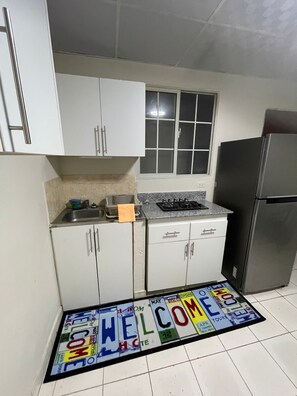 A small kitchen with white cabinets, a stainless steel refrigerator, a window, and a welcome mat. - Private room in Panama City, near the airport (Panama)